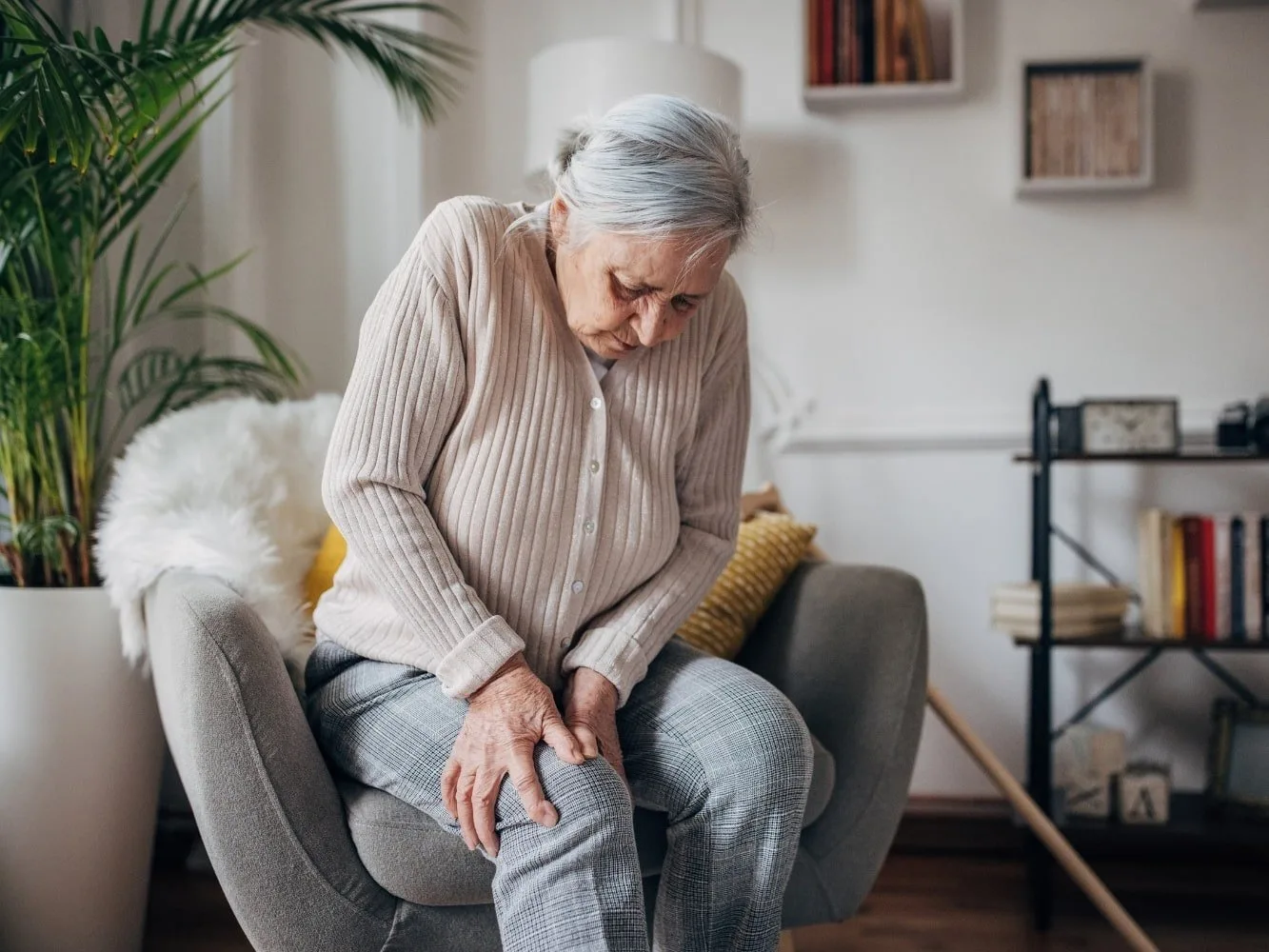 femme âgée assise sur un siège et souffrant de douleurs musculaires inexpliquées dans les bras et les jambes